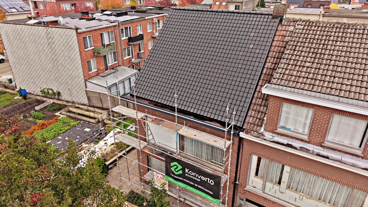 Dakrenovatie in Wilrijk: het nieuwe donkere pannendak naast het oude dak van de buren, met stelling en spandoek van Konverto