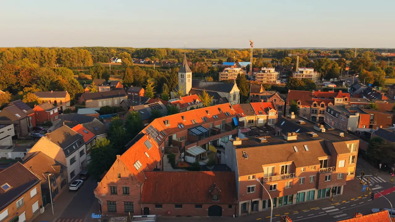Eppegem in het gouden avondlicht: over de daken naar de kerktoren, de Zenne met de voetbrug, en rond de Sint-Clemenskerk